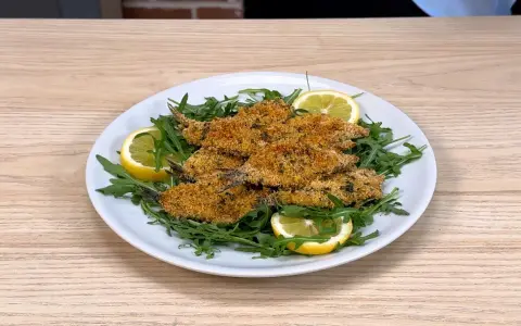Piatto di alici al forno dorate e croccanti, servite su un letto di rucola fresca con spicchi di limone.