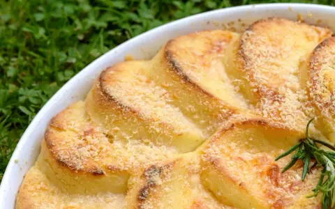 Gnocchi alla romana dorati e gratinati in una teglia bianca, con un rametto di rosmarino.