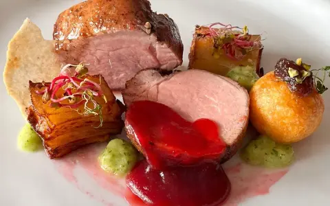 Piatto gourmet con filetto di maiale, patate croccanti, salsa rossa e guarnizioni verdi. Un'idea per le tue ricette di filetto di maiale.