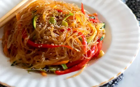 Deliziosi spaghetti di soia con verdure colorate, peperoni rossi, zucchine e carote, guarniti con semi di sesamo.