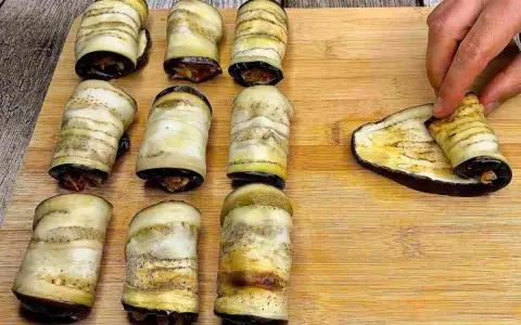 Involtini di melanzane pronti per essere infornati. Una mano sta arrotolando l'ultima fetta di melanzana grigliata.