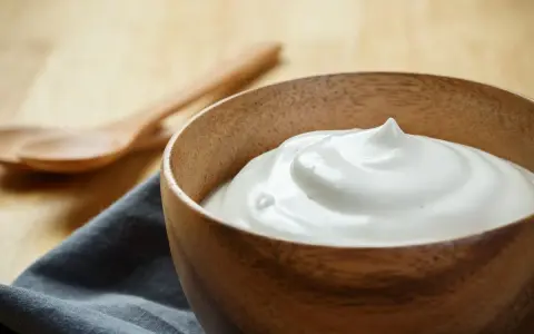 Una ciotola di legno piena di soffice crema al latte, pronta per essere gustata con due cucchiai in legno sullo sfondo.