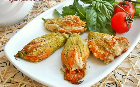 Deliziosi fiori di zucca al forno ripieni, serviti su un piatto bianco con pomodorini e basilico fresco.