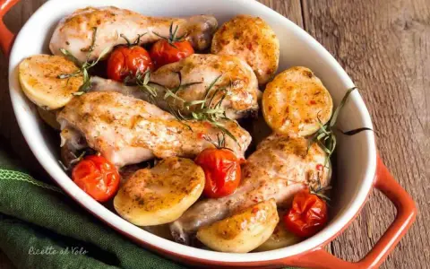 Delizioso pollo al forno con patate e pomodorini, guarnito con rosmarino fresco. Un piatto invitante e saporito.