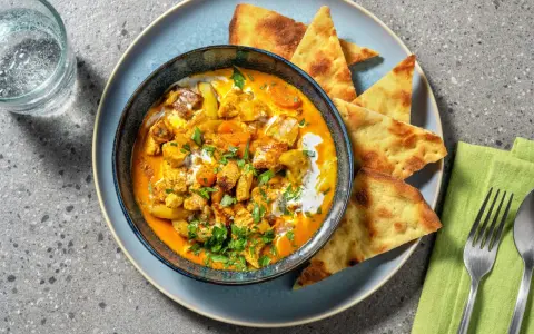 Un invitante pollo al curry cremoso, guarnito con coriandolo fresco e servito con pane naan croccante.