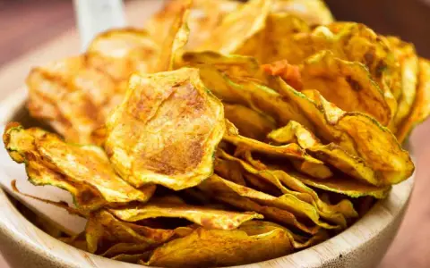 Croccanti chips di zucchine dorate, perfette per uno snack sano e gustoso, servite in una ciotola di legno.