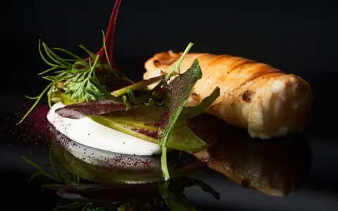 Spiedini di pesce avvolti in pasta sfoglia, serviti con una crema bianca e insalata fresca, su sfondo nero.