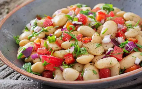 Insalata di fagioli bianchi, pomodori, cipolla rossa e erbe fresche in una ciotola rustica. Un piatto leggero e saporito.