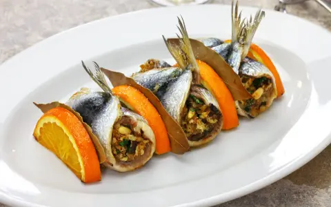 Sarde a beccafico, un piatto siciliano con sardine ripiene, arancia e alloro, servite su un piatto bianco.