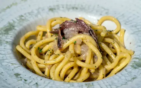 Un piatto di bigoli in salsa, pasta spessa condita con acciughe e cipolla, guarnita con prezzemolo tritato.