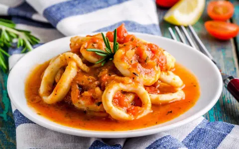 Calamari in umido succulenti, cotti in una salsa rossa saporita, guarniti con rosmarino fresco.