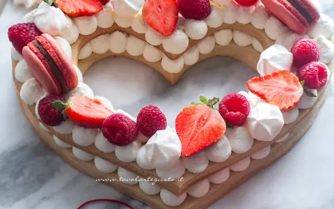 Deliziosa cream tart a forma di cuore per bambini, decorata con fragole, lamponi, meringhe e macarons.