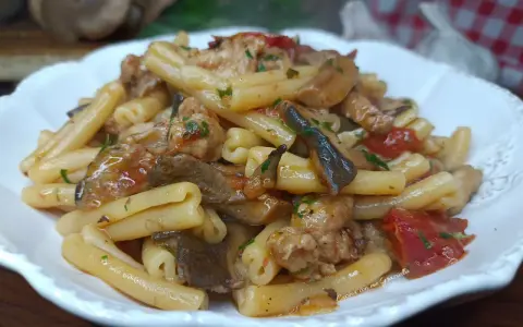 Un piatto invitante di pasta funghi e salsiccia, condita con pomodoro e prezzemolo, pronta per essere gustata.
