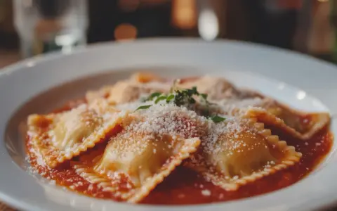 Deliziosi ravioli fatti in casa, conditi con sugo rosso, parmigiano grattugiato e un rametto di erbe aromatiche.