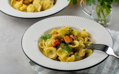 Orecchiette con patate e cozze, un piatto cremoso e saporito, guarnito con prezzemolo fresco.