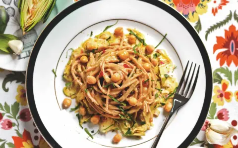 Un piatto invitante di pasta con carciofi alla siciliana, arricchito da ceci e erbe fresche, su un tovagliolo colorato.