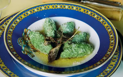 Strangolapreti alla trentina, verdi e saporiti, serviti in un piatto blu decorato con burro fuso e parmigiano.