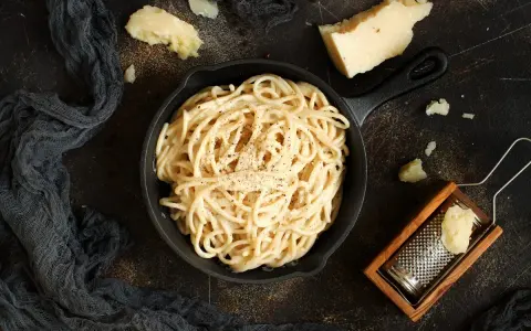 Un piatto di spaghetti cacio e pepe fumante, con pezzi di pecorino e una grattugia in legno.
