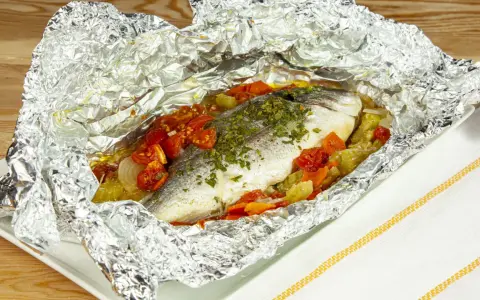 Orata al cartoccio con pomodorini e verdure, cotta al forno e servita in un foglio d'alluminio aperto.