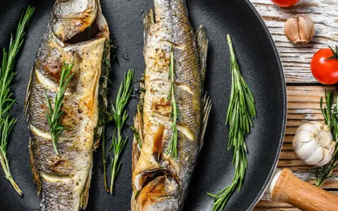 Due branzini dorati in padella, profumati al rosmarino, pronti per essere gustati.