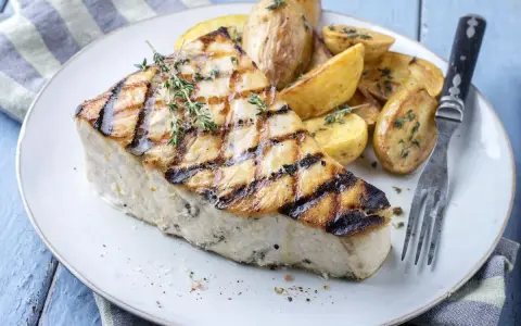 Un succulento trancio di pesce spada alla griglia, guarnito con timo fresco, servito con patate arrosto. Un'idea per le tue prossime ricette di pesce spada.