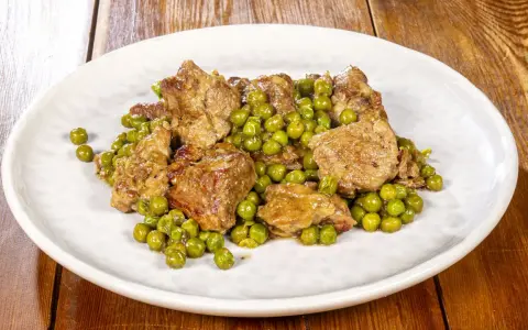 Un saporito agnello con piselli, un classico piatto italiano, servito su un piatto bianco.