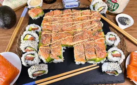 Un invitante sushi fatto in casa con salmone, avocado e formaggio Philadelphia, guarnito con semi di sesamo e una salsa cremosa.