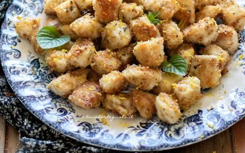 Bocconcini di pollo dorati e croccanti, guarniti con scorza di limone e foglie di menta fresca su un piatto decorato.