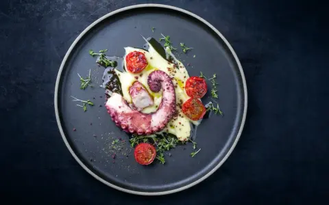 Un tentacolo di polpo alla griglia, servito su purè di patate con pomodorini confit e timo fresco.