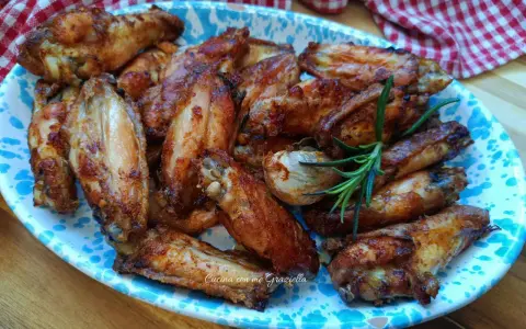 Alette di pollo dorate e croccanti, servite su un piatto decorato con un rametto di rosmarino.