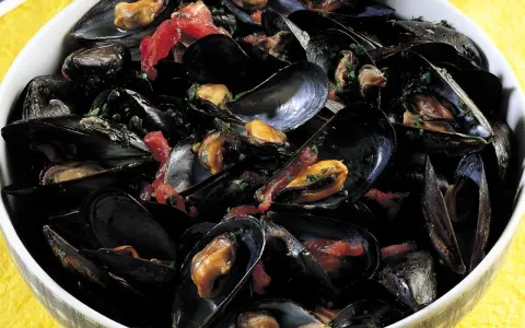 Una ciotola piena di saporita zuppa di cozze, con cozze nere aperte che rivelano la polpa succulenta, condita con erbe fresche e pomodoro.