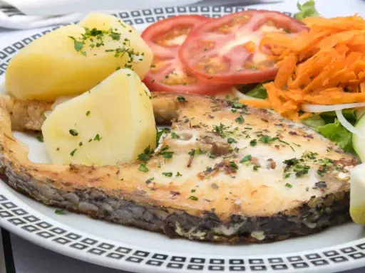 Un succulento pesce spada al forno, accompagnato da patate bollite, pomodori freschi, carote grattugiate e un'insalata leggera.