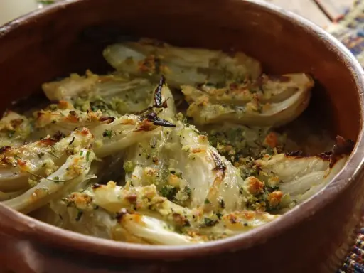 Finocchi al forno dorati e croccanti, conditi con erbe aromatiche e pangrattato, serviti in una terrina di terracotta.