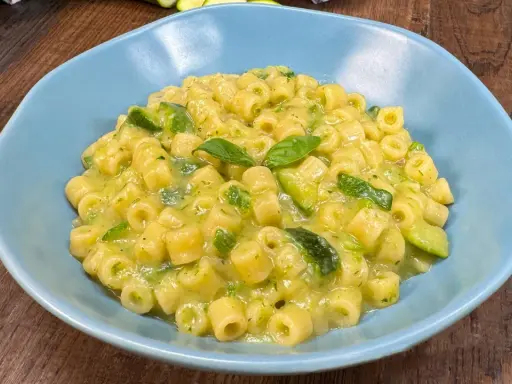 Un piatto di pasta con zucchine e basilico, cremoso e invitante, servito in una ciotola azzurra su un tavolo di legno.