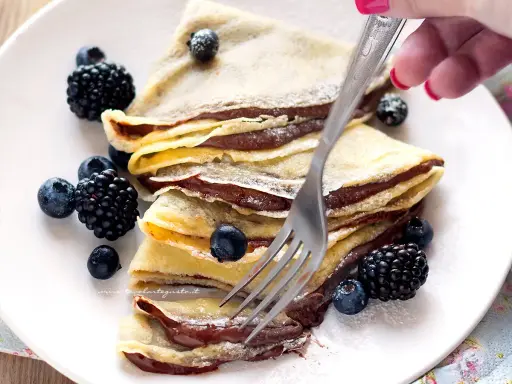 Piatto di crepes alla Nutella, guarnite con mirtilli e more, pronte per essere gustate.