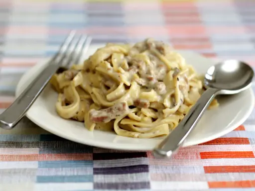 Un piatto di tagliatelle ai funghi cremose, con forchetta e cucchiaio pronti per gustare questo delizioso primo.