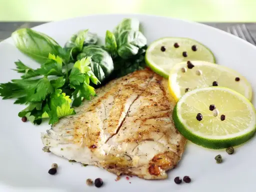 Un delizioso filetto di pesce san pietro grigliato, guarnito con erbe fresche, fette di limone e lime con pepe nero.