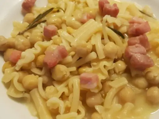 Piatto di pasta e ceci in scatola, con cubetti di pancetta e un rametto di rosmarino.
