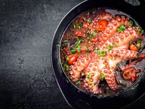 Polpo alla luciana in padella, con pomodorini e prezzemolo fresco. Un piatto succulento e profumato, pronto per essere gustato.