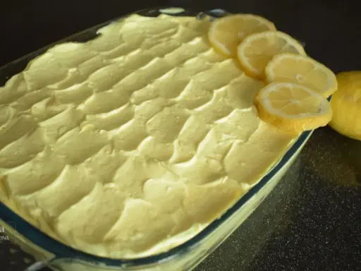 Un invitante tiramisù al limone, guarnito con fette di limone fresco e limoni interi, pronto per essere gustato.