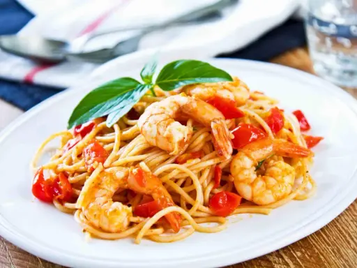 Spaghetti con gamberetti succulenti, pomodorini freschi e basilico, un piatto invitante pronto per essere gustato.