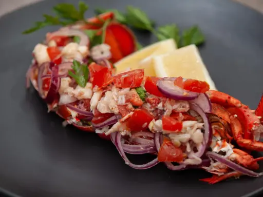 Astice alla catalana: un piatto fresco con astice, pomodoro, cipolla rossa e limone, guarnito con prezzemolo.