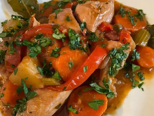 Un saporito spezzatino di pollo con carote, peperoni rossi e prezzemolo tritato, servito in un piatto bianco.