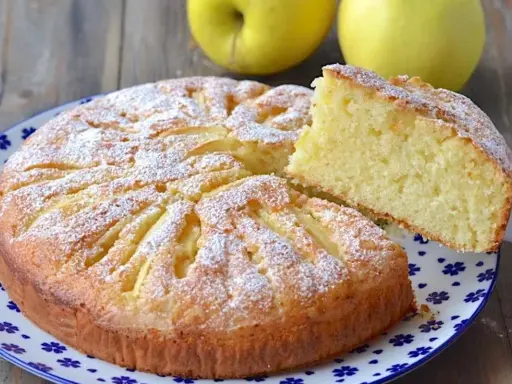Deliziosa torta di mele con yogurt, cosparsa di zucchero a velo, con una fetta sollevata per mostrare la morbidezza.
