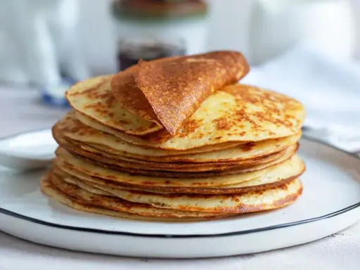 Una pila di dorate crepes senza glutine, una piegata in cima, su un piatto bianco.