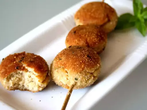 Polpette tonno e ricotta dorate su uno spiedino, una è stata morsa, con basilico fresco.