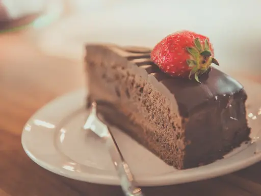 Una fetta di torta al cioccolato, ricoperta di glassa lucida e guarnita con una fragola fresca, pronta per essere gustata.