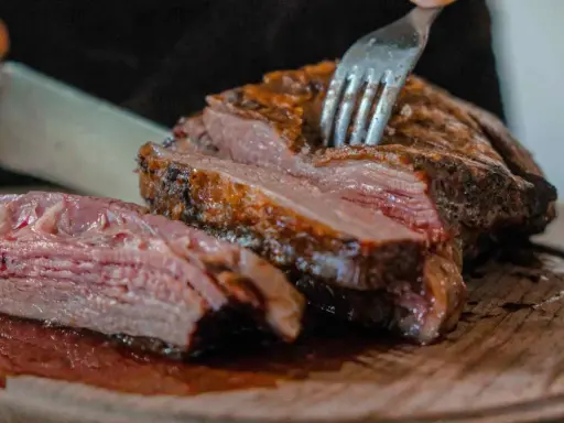Un succulento arrosto di maiale, tagliato a fette su un tagliere di legno, con una forchetta che affonda nella carne tenera.