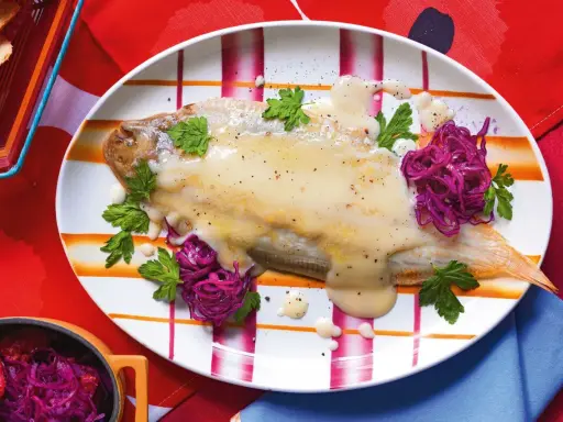 Sogliola alla mugnaia su piatto a righe, guarnita con cavolo rosso e prezzemolo.