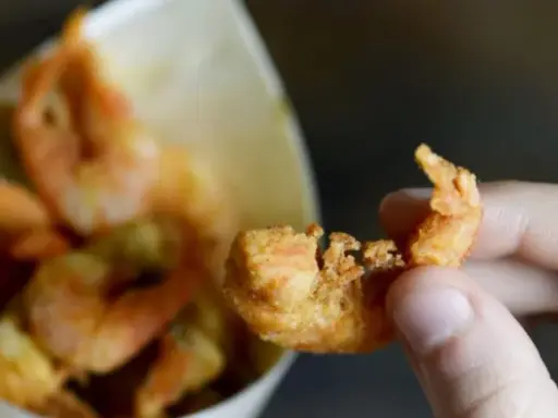 Una mano tiene un gambero croccante, parte di una deliziosa frittura di pesce servita in un cono di carta.